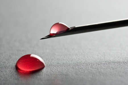 The Sharp point from a medical injection needle with a droplet of blood on gray surfaceの写真素材