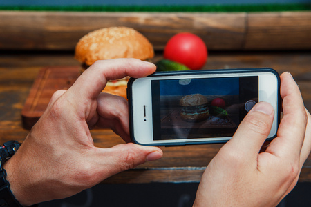 Man takes a picture smartphone eating fast food. Delicious homemade burgers.の写真素材
