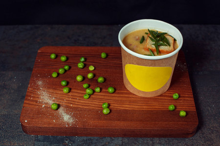 Pea soup in a paper cup. The soup stands on the board, and peas are peeled around it.の写真素材