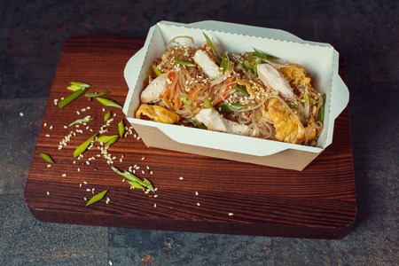 Concept of street food. Chinese Japanese noodles with chicken and vegetables in disposable paper utensils. Copy space, selective focusの写真素材