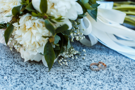 Photo image of a classic wedding gold rings of the bride and groom on a white table, with a beautiful wedding bouquet of flowers of the brideの写真素材