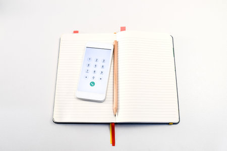 Smartphone and pencil in the book on the white table, ready for call and ready for noteの写真素材