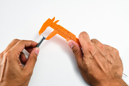 Hold the vernier caliper and open jaw to measure a  diameter of head knot screw. All are done on the white tableの写真素材