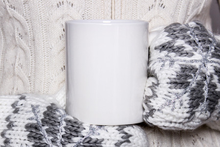 Girl in a warm clothes and mittens is holding white mug in hands. Mockup for winter gifts design, Merry Christmas and Happy New Year.の写真素材