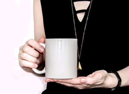 Girl in black dress is holding white cup, mug in hands. Mockup for designs.の写真素材