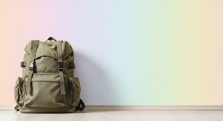 Green backpack on a wooden floor in front of a colored wall.の素材