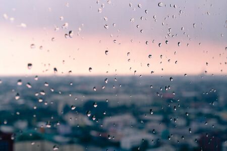 Water droplets on office building window with vivid city sunset blurred backgroundの写真素材