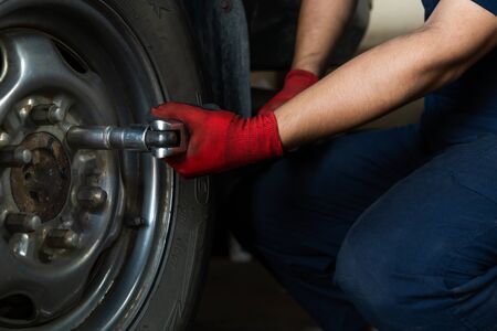 Automotive engineer operating hand tools on car in repair centre, while replacing wheel and tires - Maintenance technician servicing truck during routine vehicle service inspectionの写真素材
