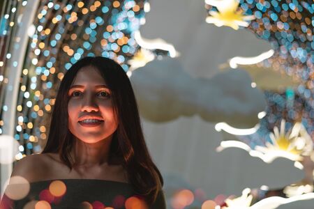 Young diverse woman smiling alone at night surrounded by colourful neon bokeh lights - Cute hipster...