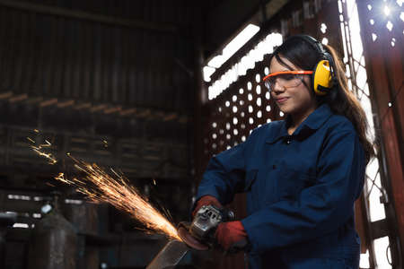 Young diverse female mechanic using factory equipment to cut metal wearing safety workwear and...