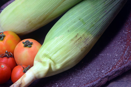 corn and tomatoes on a wooden cutting board, closeup of photoの写真素材