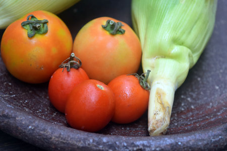 tomatoes and corn in a clay bowl on a wooden table.の写真素材