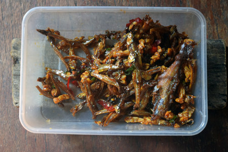 Fried fish with spicy sauce in plastic container on wooden background.の写真素材