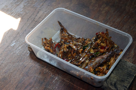Fried fish with spicy sauce in a plastic container on wooden tableの写真素材