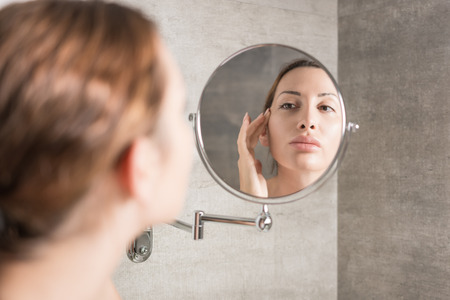 Beautiful woman without makeup, looks in the mirrorの写真素材