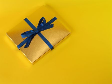 Close up view of a gold gift box with blue bow on bright yellow background, with copy space