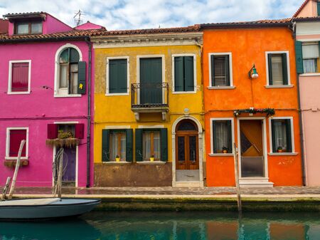 The colorful, brightly painted houses on the Venetian island of Burano. A boat is moored on the canal. Burano, Venice - Italyの写真素材