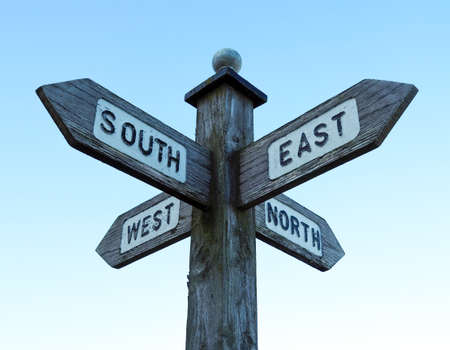 Wooden directional sign post displaying the compass points North, East, South, West. Set against a clear, pale blue skyの写真素材