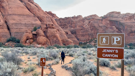 A female hiker on the trail for Jennys Slot Canyon with red rock Navajo sandstone cliffs in the background and trailhead sign in the foreground - Snow Canyon State Park, St George, Utahの写真素材