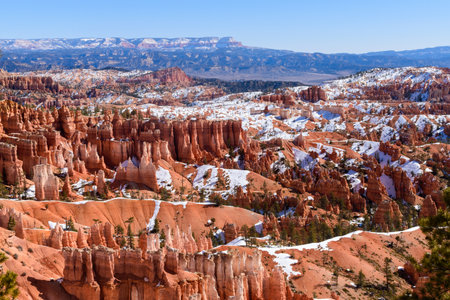 Breathtaking panoramic view of Bryce Canyons Amphitheater from the Queens Garden Trail. Vibrant red rock hoodoo formations contrast with patches of snow under a clear, blue sky - Utah, USAの写真素材