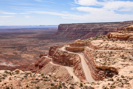 Beautiful scenic view of the winding and steep Moki Dugway Road in Utah, USA. The landscape of red rock formations and a car traversing the road showcases the stunning natural beauty of the region.の写真素材