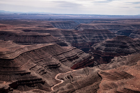 Stunning aerial view from the dramatic Muley Point overlook into canyons and the winding San Juan River in Utah, USA. The rugged landscape showcases geological formations and the vast desert.の写真素材
