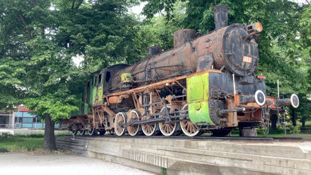 Historical steam engine locomotive in an outdoor park surrounded by lush green foliage. Represents...