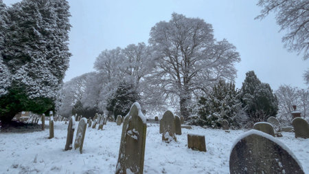 A serene winter scene capturing an old graveyard covered in snow, with icy trees and quiet surroundings. The atmosphere combines tranquility and reverence in this picturesque view of the cemetery - UKの写真素材