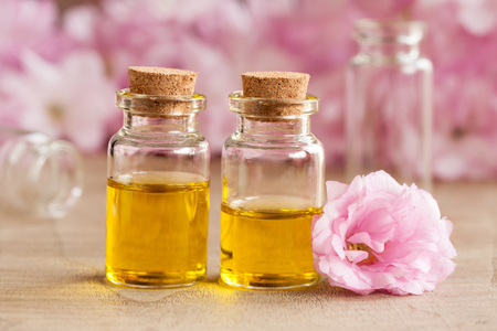 Two bottles of essential oil with pink japanese cherry blossoms in the backgroundの写真素材