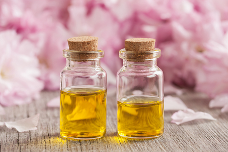Two bottles of essential oil with pink cherry blossoms in the backgroundの写真素材