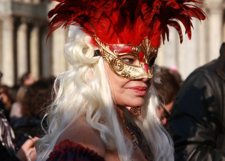 Woman in a costume and mask with red feathers at the carnival in Venice, Italy, in front of the Basilica San Marco, 6th March 2011.のeditorial素材