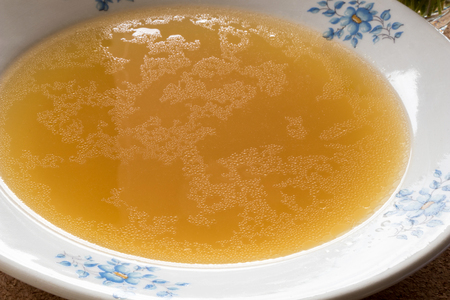 Bone broth made from chicken, served in a vintage white plate with blue flower ornamentsの写真素材
