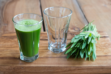 Green barley grass shot in a glass, with blades of young barley on a wooden backgroundの写真素材