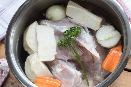 Ingredients for preparing chicken bone broth in a pot - chicken, onions, celery root, carrots, parsleyの写真素材