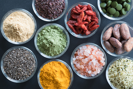Selection of superfoods on a black background - goji berries, chlorella, young barley powder, dulse seaweed, maca, chia seeds, turmeric, himalayan sea salt, hemp seeds, raw cocoa nibsの写真素材