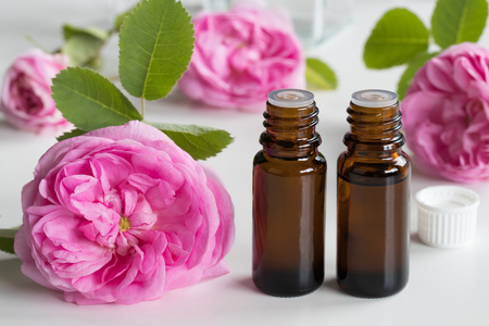 Two bottles of rose essential oil with rose flowers on a white backgroundの写真素材