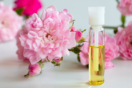 A bottle of rose essential oil with small rose blossoms on a white backgroundの写真素材