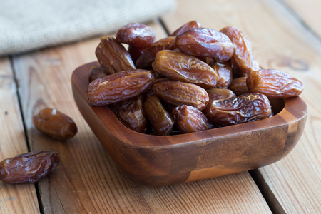 Dried dates in a bowl on a wooden table.の写真素材