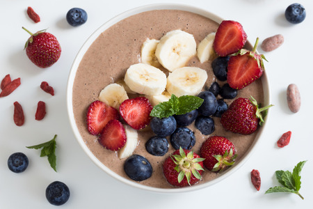 Summer breakfast: raw breakfast bowl with strawberries, blueberries and banana on a white background, top viewの写真素材