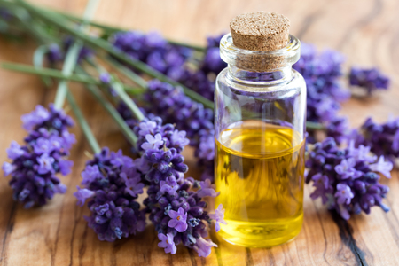 A bottle of essential oil with fresh lavender twigs on a wooden backgroundの写真素材