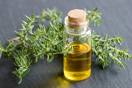 A bottle of essential oil with fresh thyme leaves on a dark backgroundの写真素材