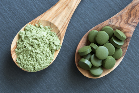 Chlorella tablets and young green barley powder on two wooden spoons on a dark backgroundの写真素材