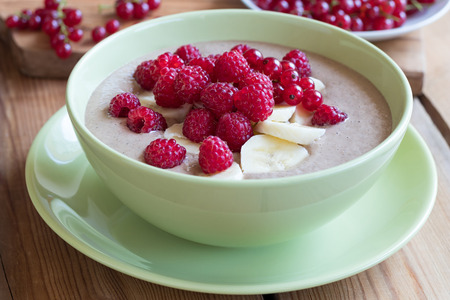Summer breakfast - raw breakfast bowl with raspberries and red currants on a wooden backgroundの写真素材