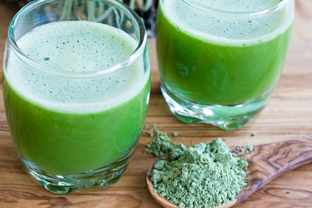 Barley grass powder on a spoon, with two fresh barley grass shotsの写真素材