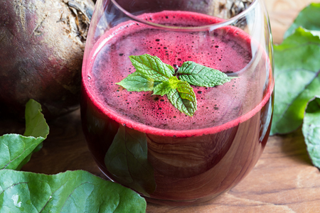 Red beet juice in a glass on a wooden background with lemon and beet greensの写真素材