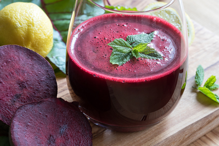Red beet juice in a glass on a wooden background with lemon and beet greensの写真素材