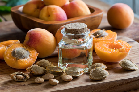 A bottle of apricot kernel oil with apricot kernels and ripe apricots on a wooden backgroundの写真素材