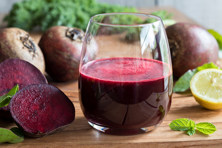 Red beet juice in a glass on a wooden background with lemon, beets and greensの写真素材