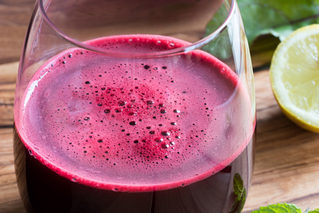 Red beet juice in a glass on a wooden background with lemon and beet greensの写真素材