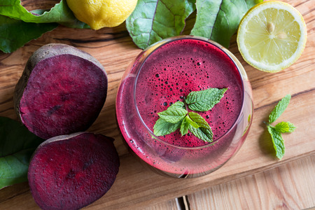 Red beet juice in a glass on a wooden background with lemon and beet greensの写真素材